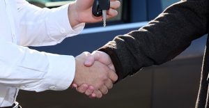 a car dealer hands over used car keys to a buyer
