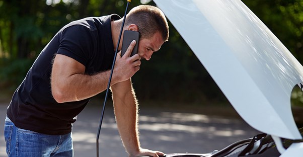 a man looks under the hood of his car while on the phone with a car warranty provider