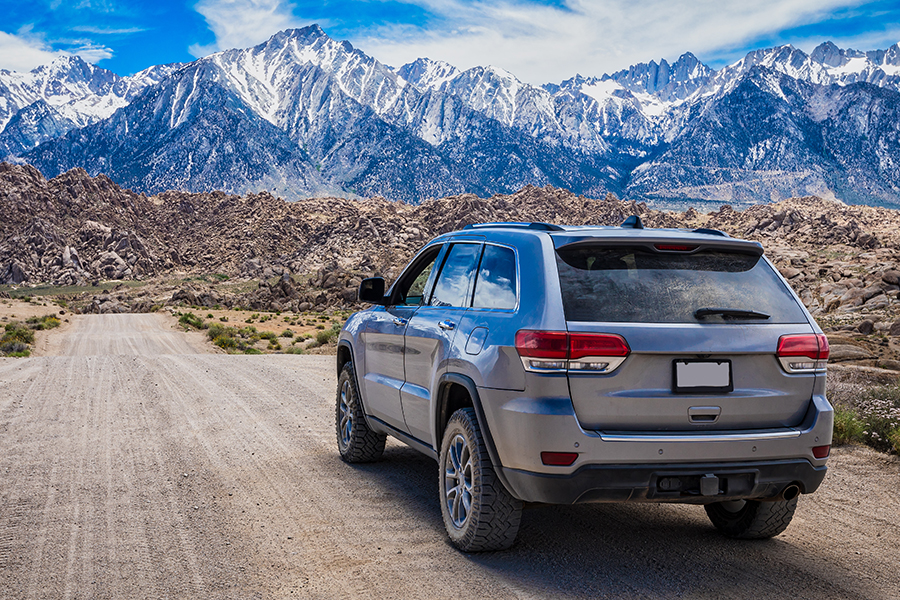 a hybrid suv drives down a dirt road toward mountains