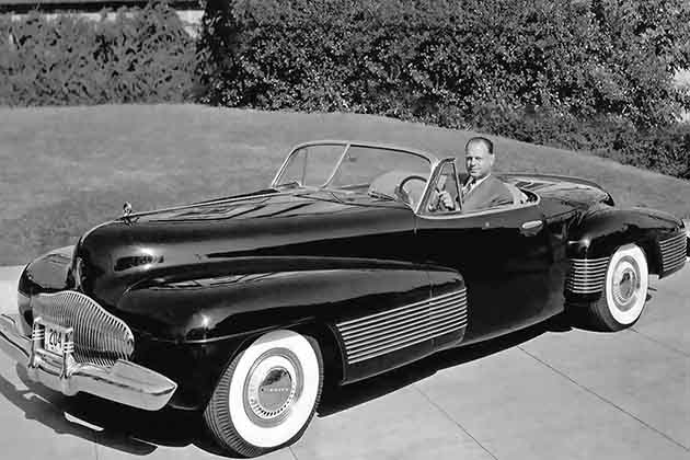 a man sitting in the 1938 buick y-job in a driveway