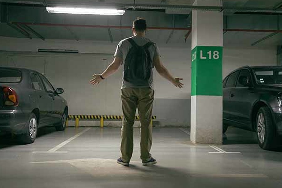 a man stands in a parking garage between two cars and decides which one to steal