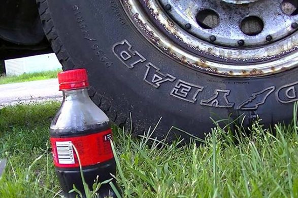 a coca cola bottle sitting beside a car tire