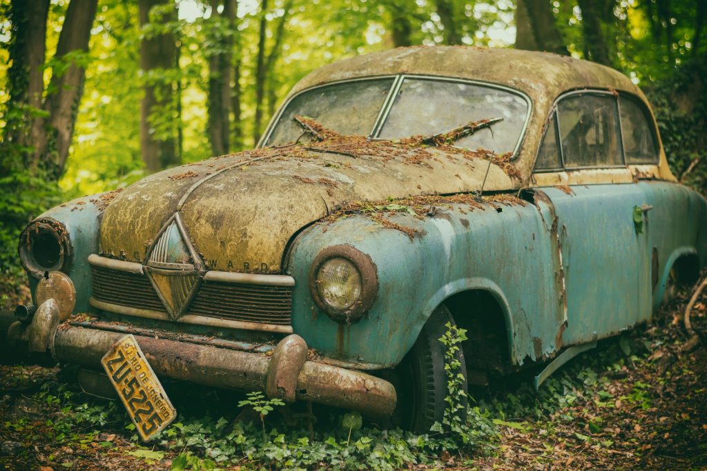 a rusted broken down car in a forest to convey the idea of least reliable