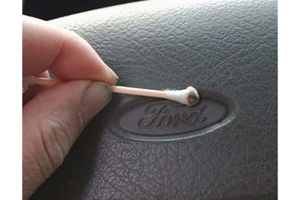 a q tip being used to clean the logo on a car steering wheel
