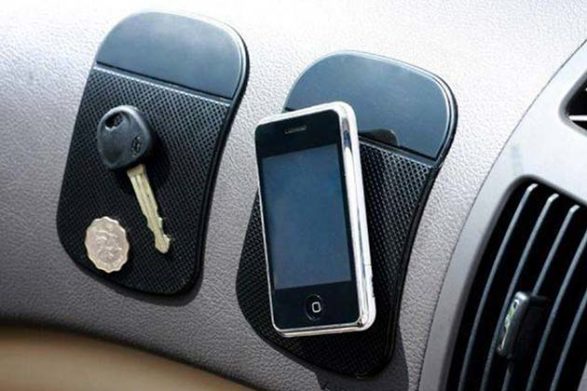 a phone a key and a coin stuck to sticky mats on a car dashboard