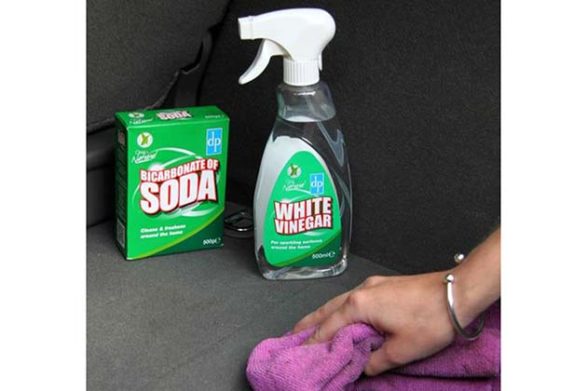 a bottle of white vinegar sitting on the floor of a car and someone wiping up a spill