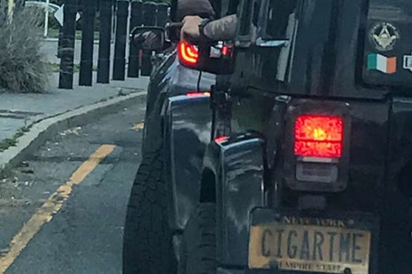 a driver holding a cigar while driving a jeep with a license plate that says CIGARTME
