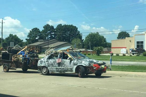 a car covered in graffiti pulling a trailer filled with lots of trash