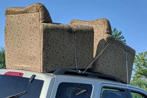two love seats on top of an suv held on only by a thin rope