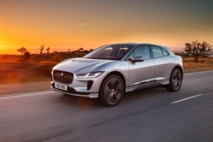 a silver 2019 jaguar i-pace driving down the road in front of a sunset