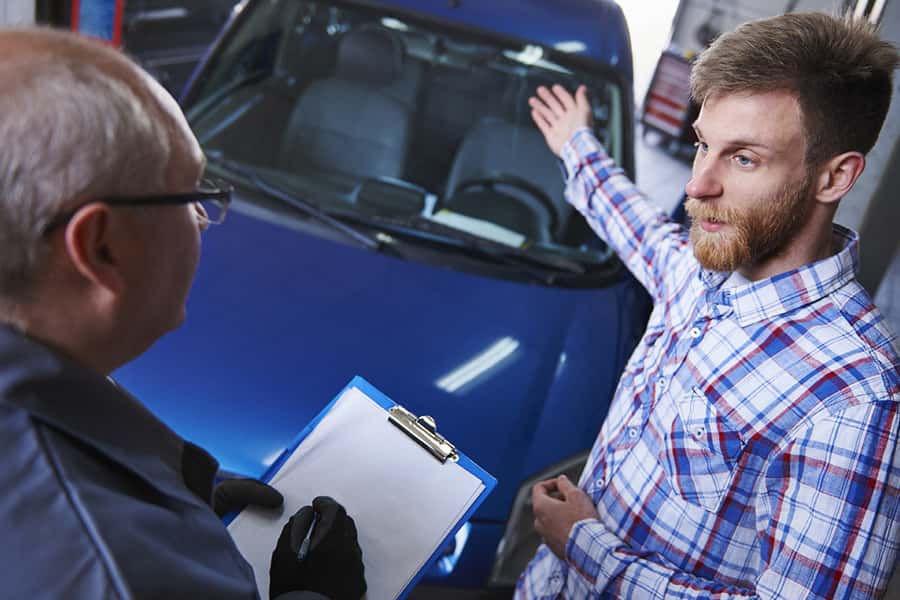 a customer and car mechanic discuss problems in front of a car