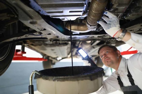 a mechanic drains the oil from the bottom of a car