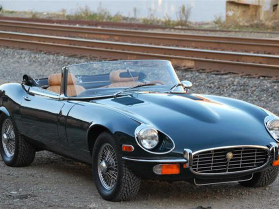 a black jaguar xk-e v12 series iii with its convertible top down and parked next to a railroad track