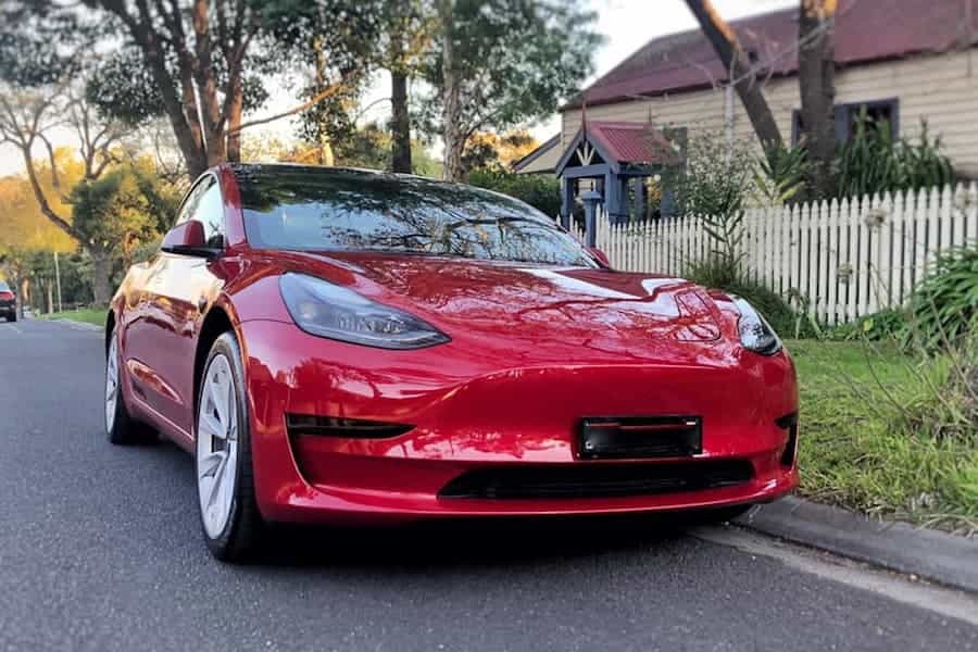 2021 red tesla model 3 parked on the street outside a house